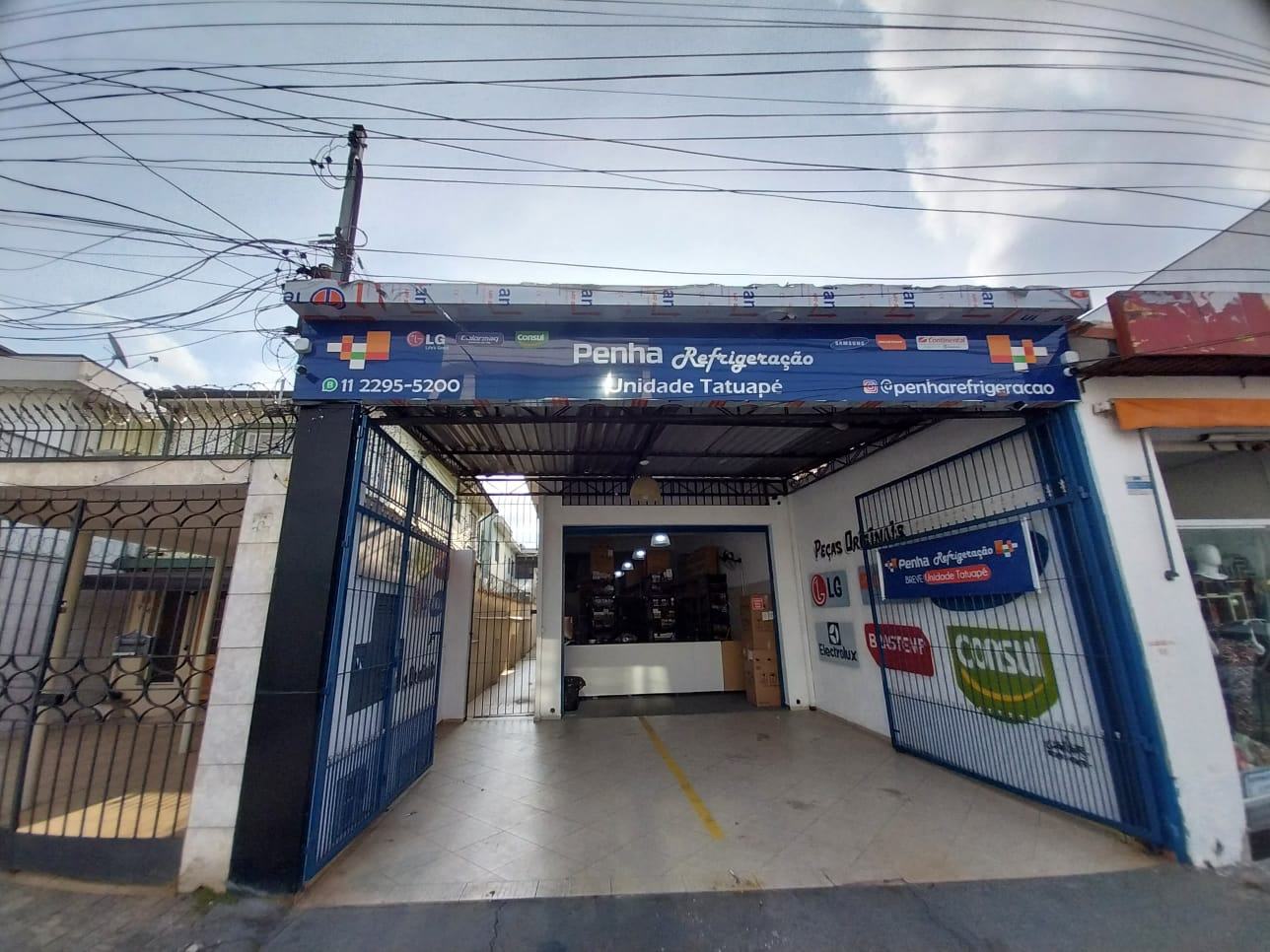 Fachada da loja: portão azul aberto sob letreiro azul escrito Penha Refrigeração Unidade Tatuapé com o telefone 11 2295-5200
